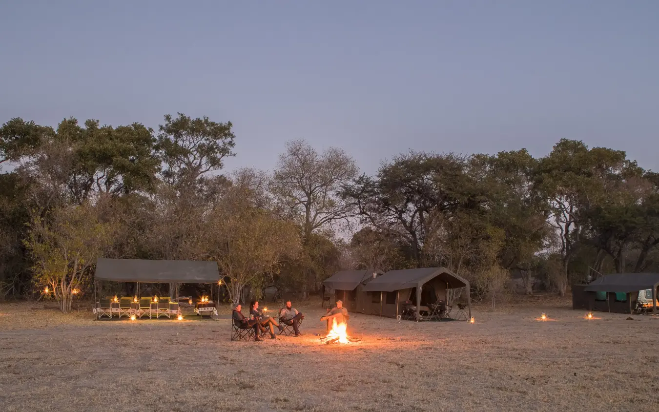 Mobile safari camp at dusk with central campfire and guests