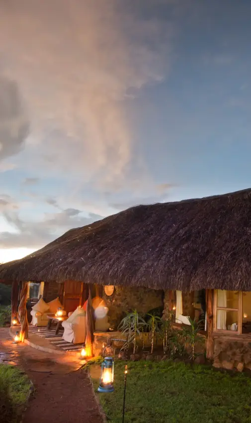 Thatched-roof lodge illuminated at dusk with savanna landscape, Lewa House, Laikipia Highlands, Kenya