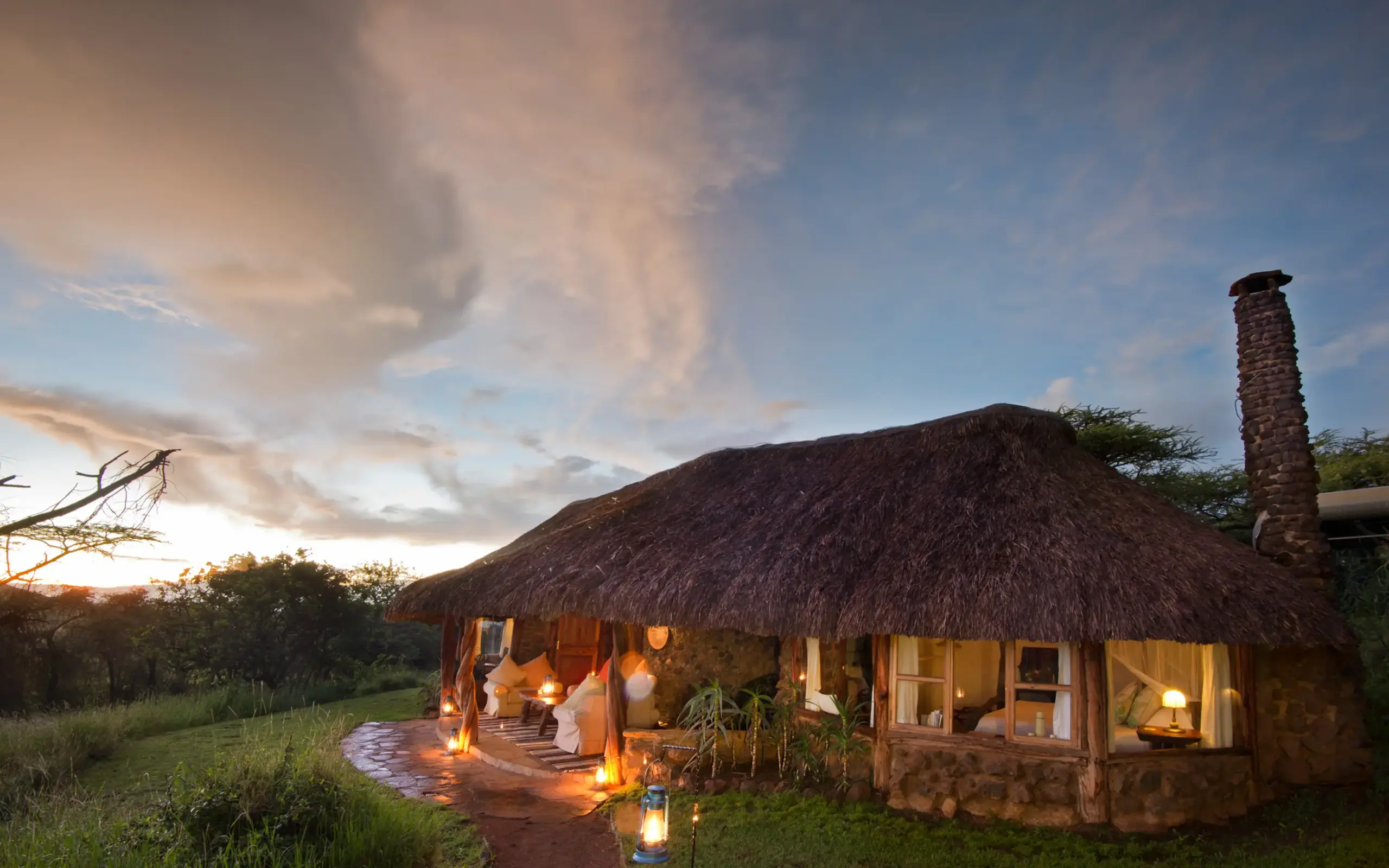 Thatched-roof lodge illuminated at dusk with savanna landscape, Lewa House, Laikipia Highlands, Kenya