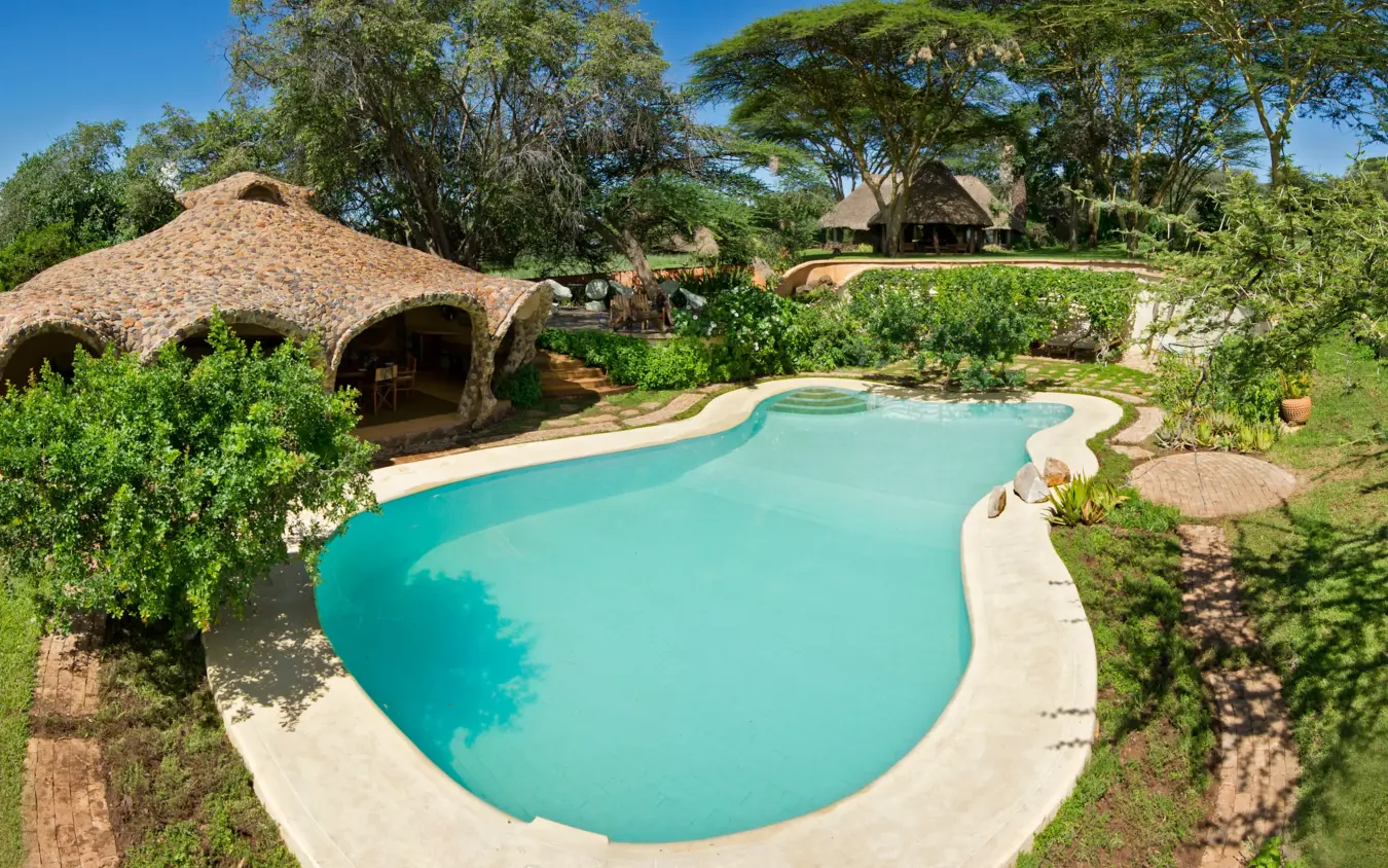 Turquoise swimming pool with thatched roof building and manicured grounds, Lewa House, Laikipia Highlands, Kenya