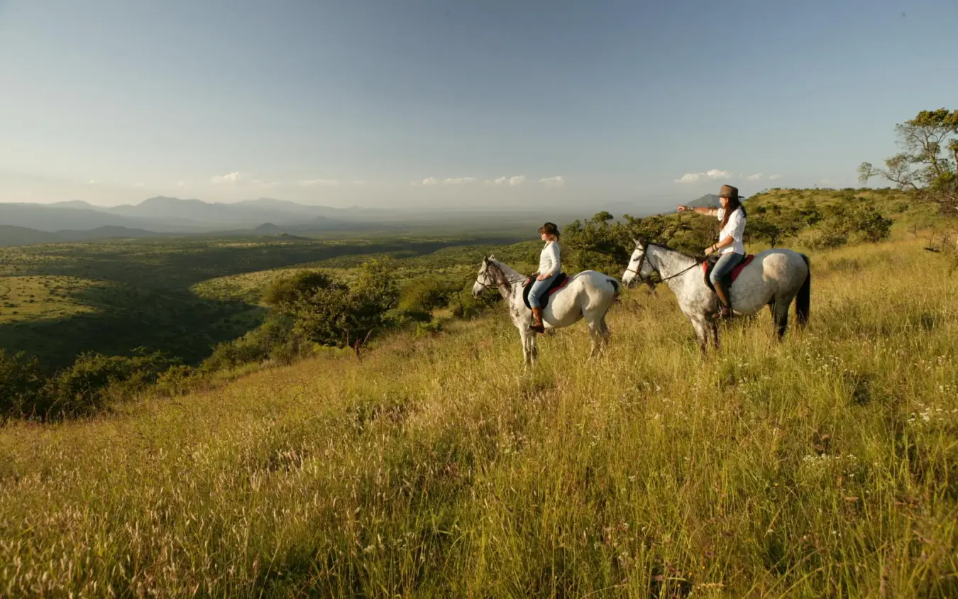 Horseback riders on grassland overlooking valley landscape, Lewa Wilderness, Laikipia Highlands, Kenya