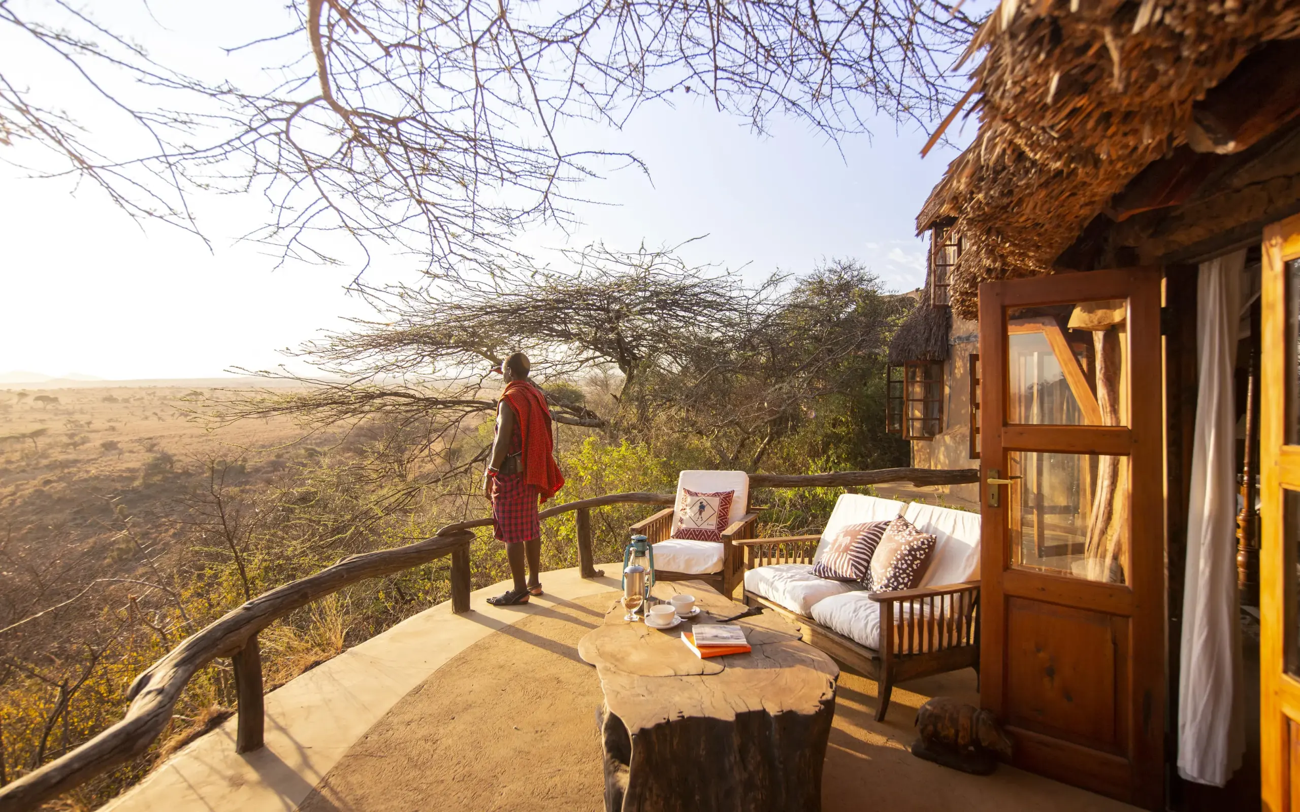 Guest relaxes on wooden deck overlooking savanna landscape, Lewa Wilderness, Laikipia Highlands, Kenya