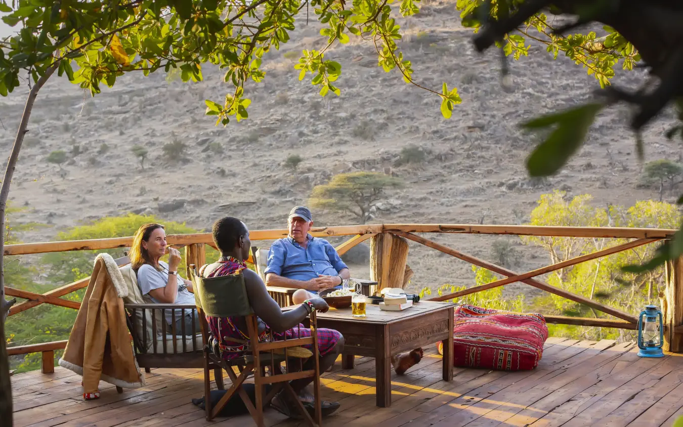 Guests relaxing on wooden deck overlooking hillside landscape, Lewa Wilderness, Laikipia Highlands, Kenya