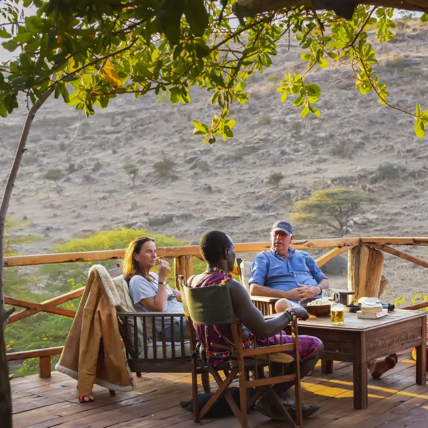 Guests relaxing on wooden deck overlooking hillside landscape, Lewa Wilderness, Laikipia Highlands, Kenya