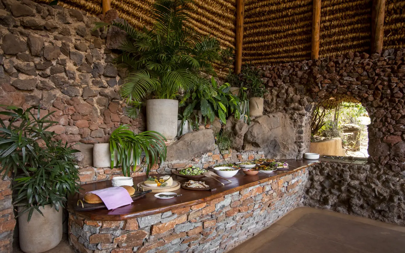 Outdoor dining setup with food and plants in stone structure, Lewa Wilderness, Laikipia Highlands, Kenya