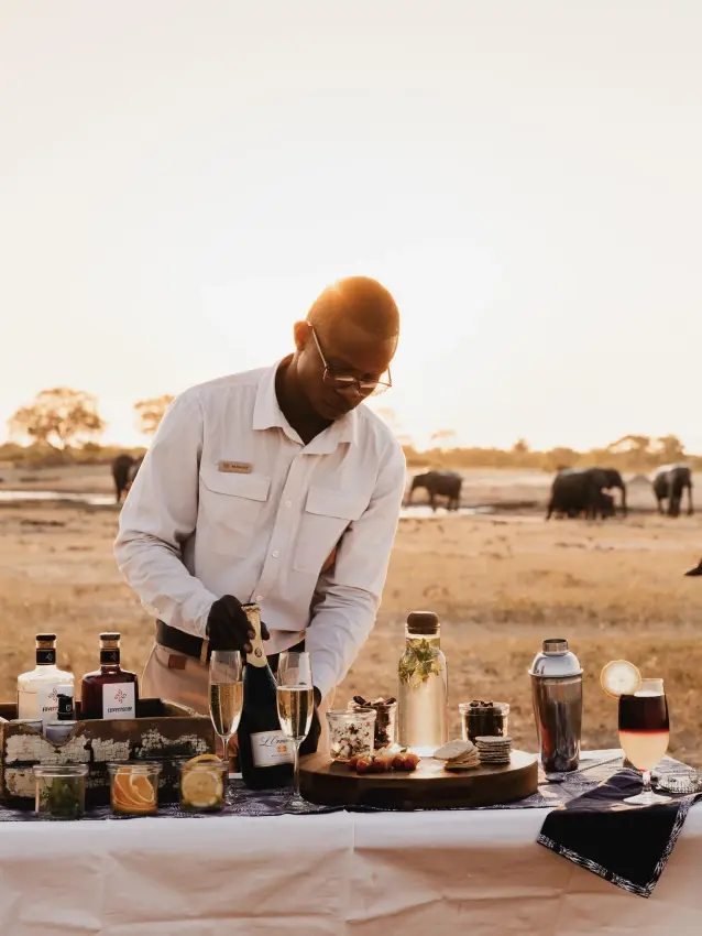 Staff member arranging beverages and supplies at outdoor table, Linkwasha Camp, Hwange National Park, Zimbabwe