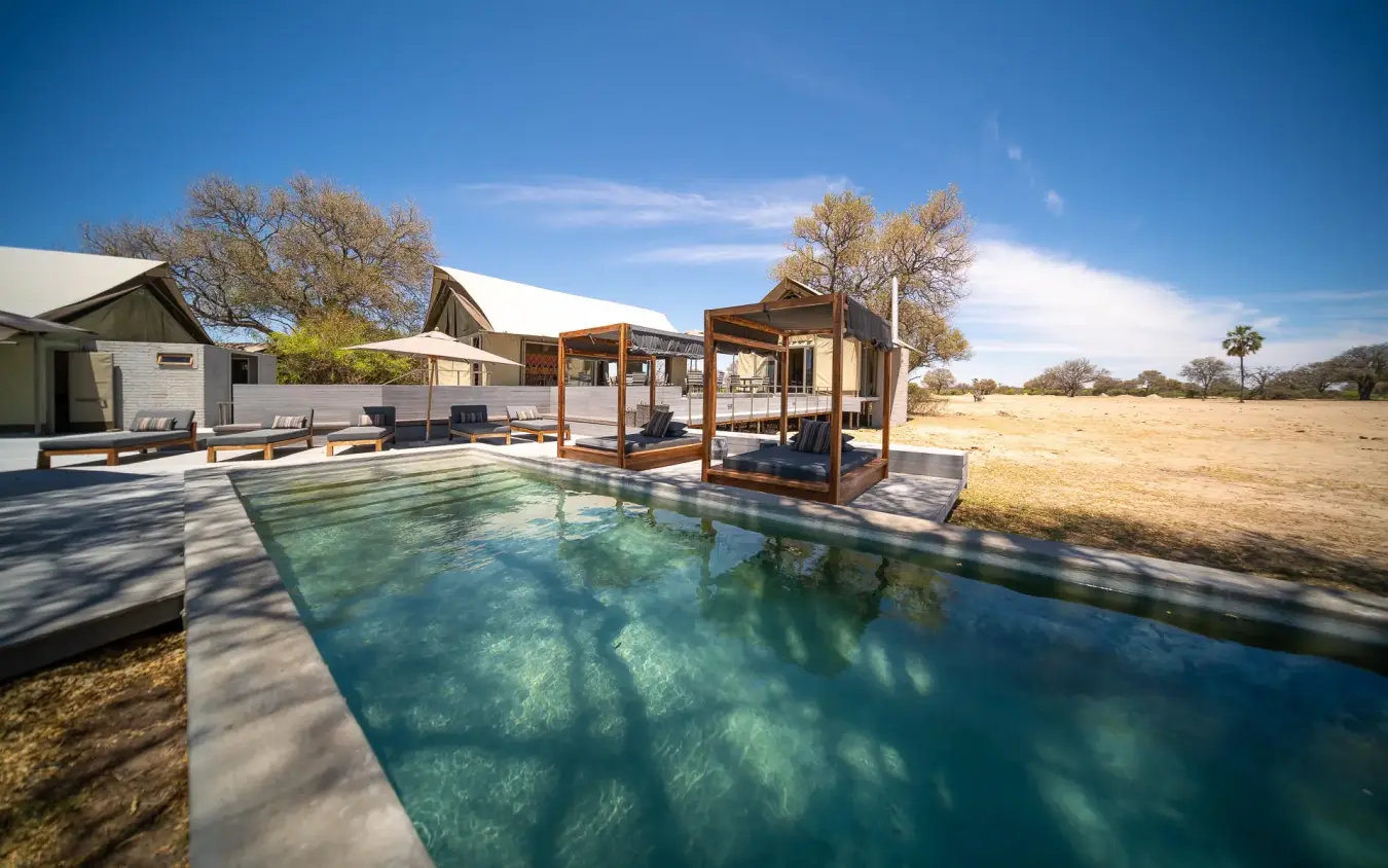 Resort pool with thatched structures and dry savanna landscape, Linkwasha Camp, Hwange National Park, Zimbabwe