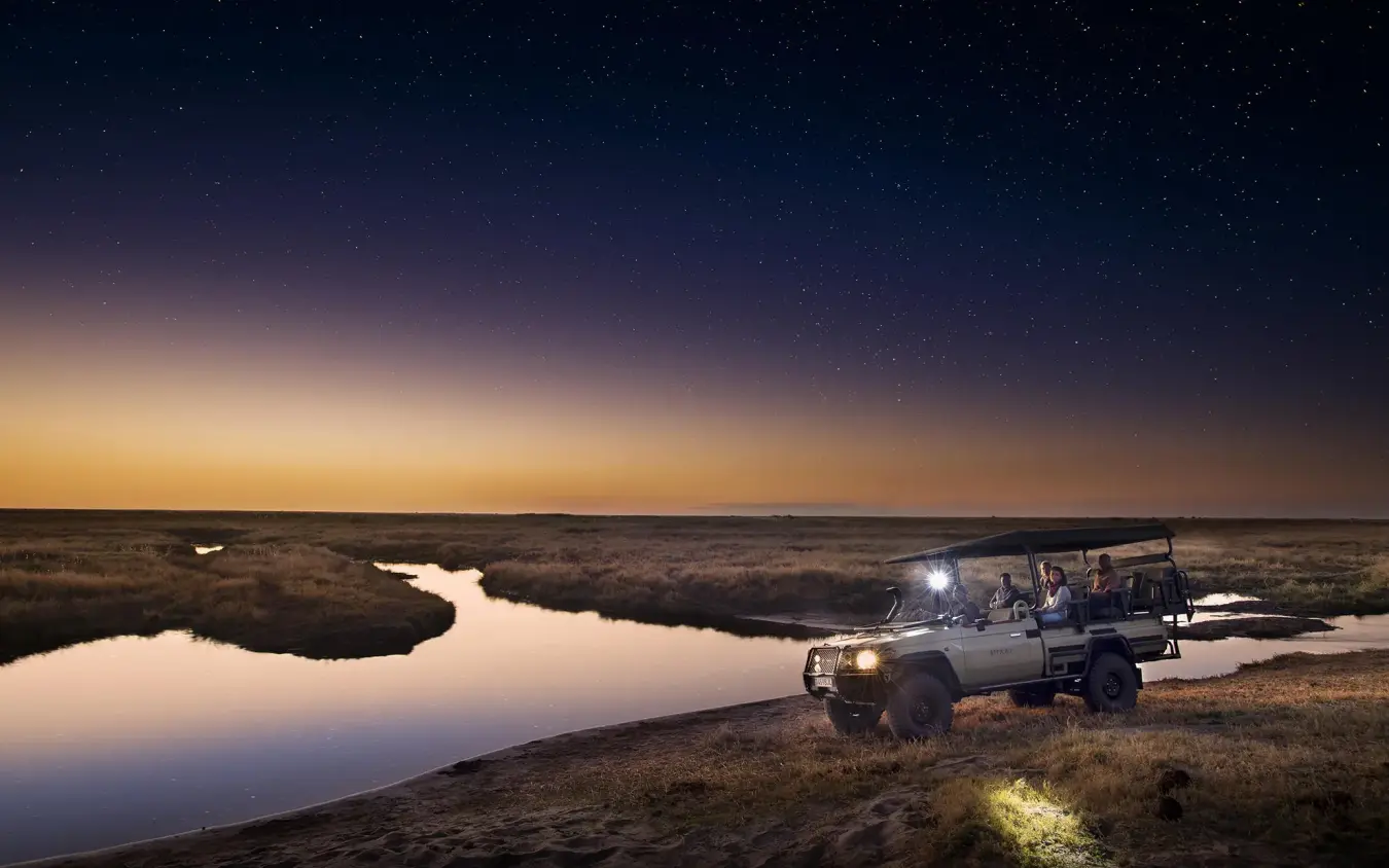 Safari vehicle on night game drive overlooking wetland at dusk, Linyanti Bush Camp, Linyanti Wildlife Reserve, Botswana