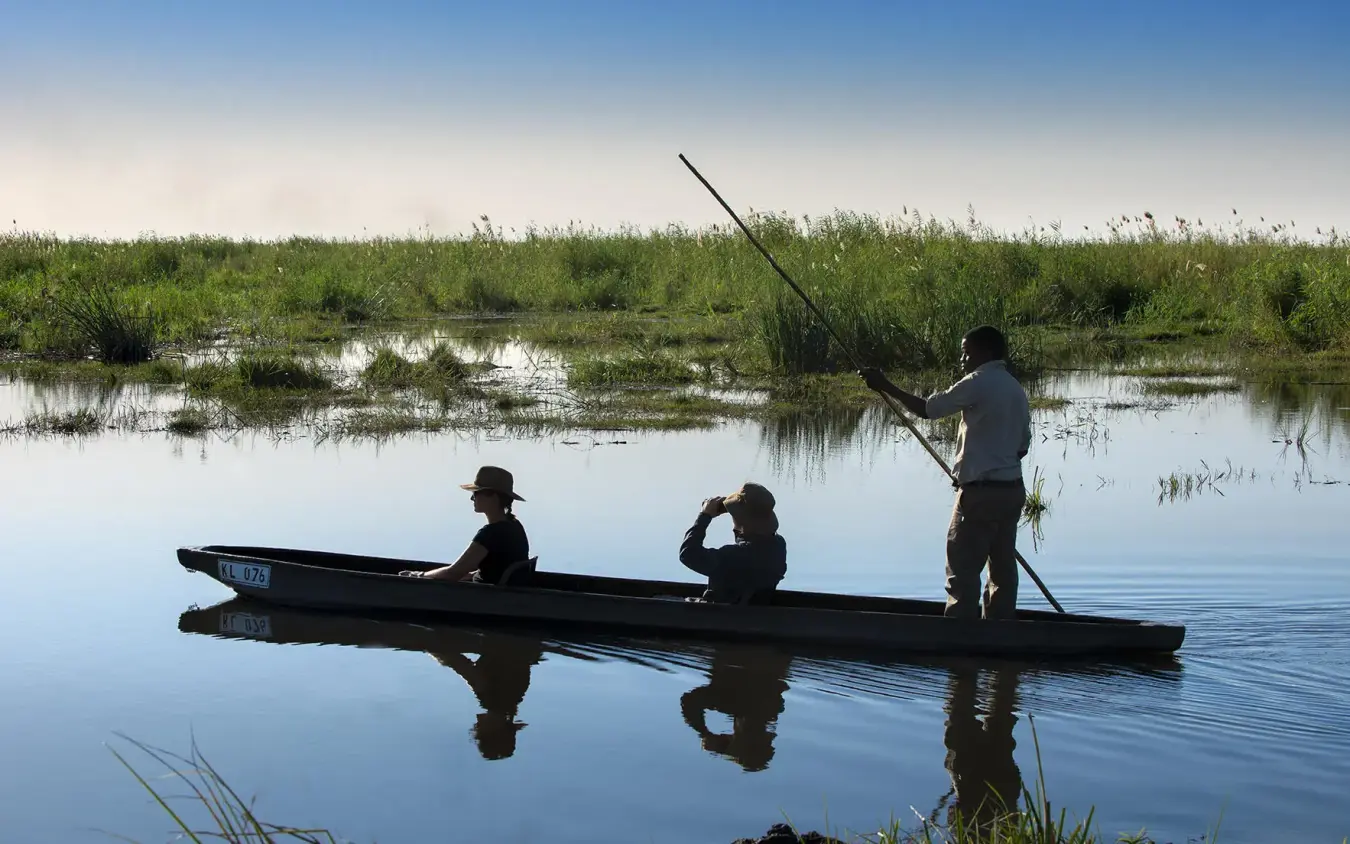 Three people poling a traditional mokoro boat through shallow water, Linyanti Bush Camp, Linyanti Wildlife Reserve, Botswana