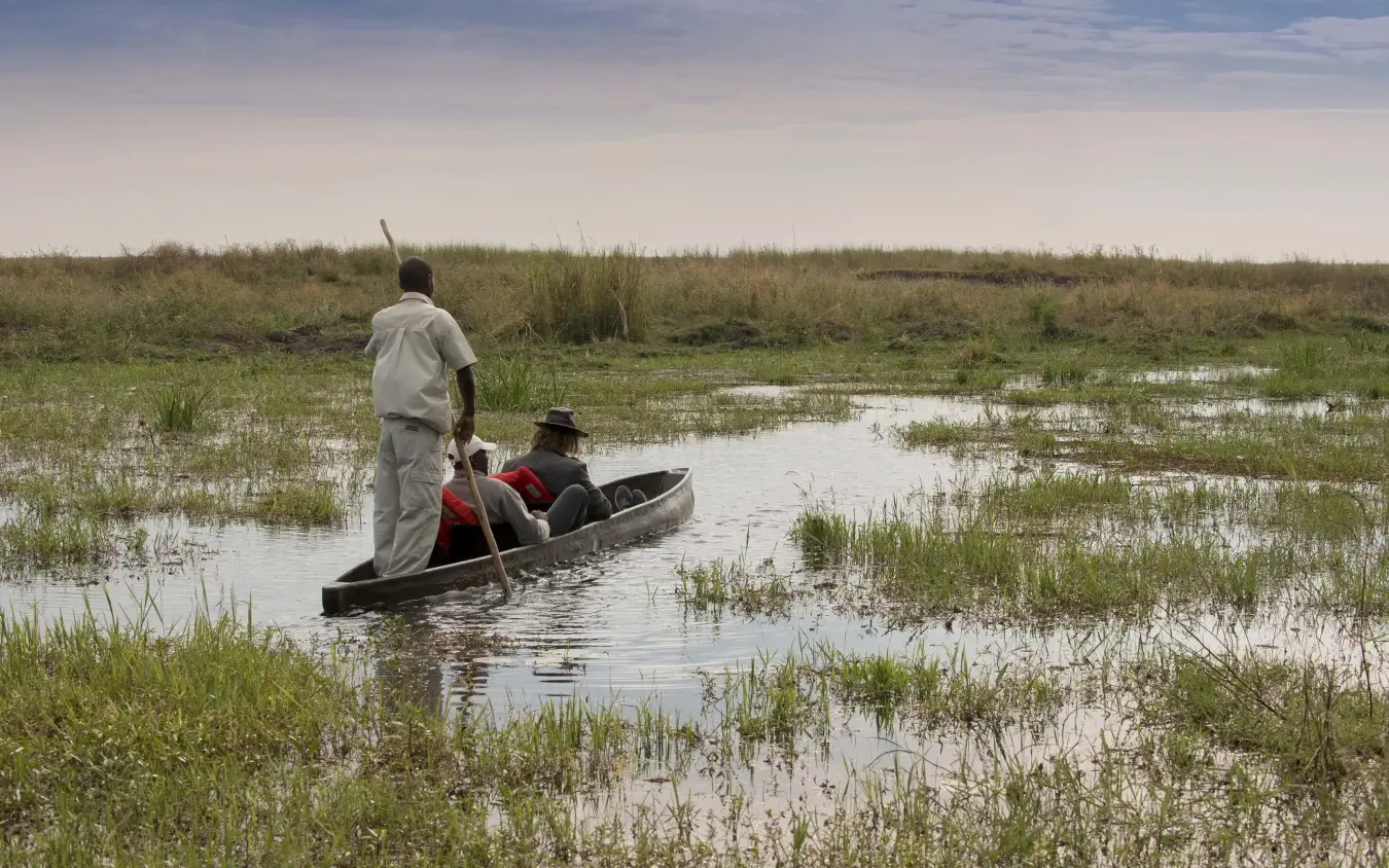 Guides poling traditional boat through wetland channels, Linyanti Bush Camp, Linyanti Wildlife Reserve, Botswana