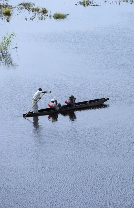 Guests in traditional wooden boat on calm water, Linyanti Bush Camp, Linyanti Wildlife Reserve, Botswana