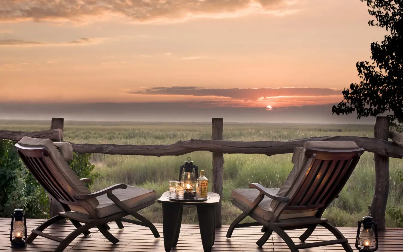 Wooden deck with lounge chairs overlooking vast savanna at sunset, Linyanti Bush Camp, Linyanti Wildlife Reserve, Botswana