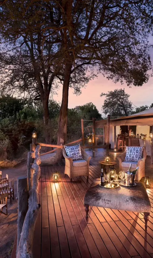 Wooden deck with seating areas overlooking savanna at dusk, Linyanti Bush Camp, Linyanti Wildlife Reserve, Botswana