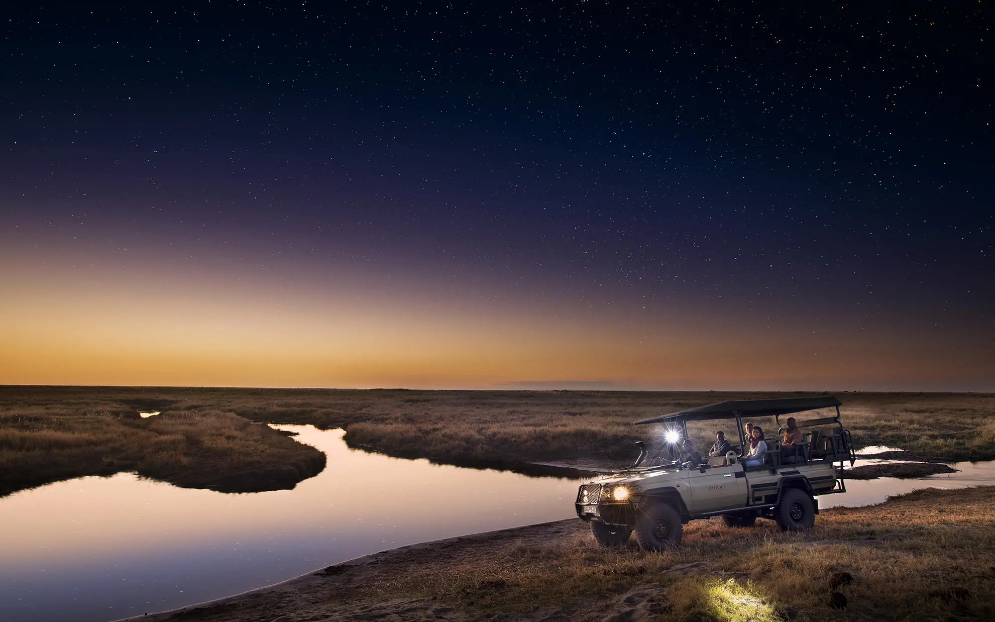 Safari vehicle on night game drive beside waterhole, Linyanti Ebony, Linyanti Wildlife Reserve, Botswana