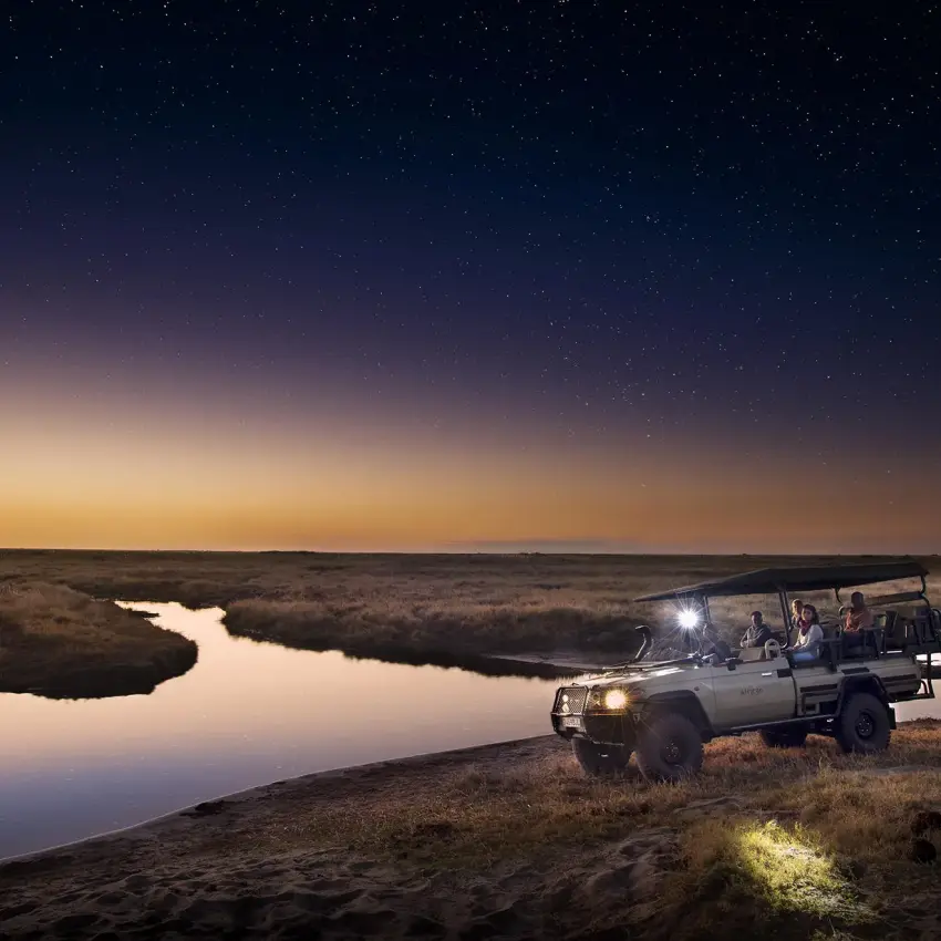 Safari vehicle on night game drive beside waterhole, Linyanti Ebony, Linyanti Wildlife Reserve, Botswana