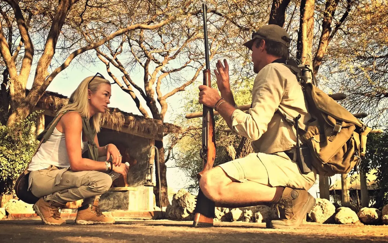 Guide demonstrating rifle to female guest under acacia trees, Little Chem Chem, Lake Manyara, Tanzania