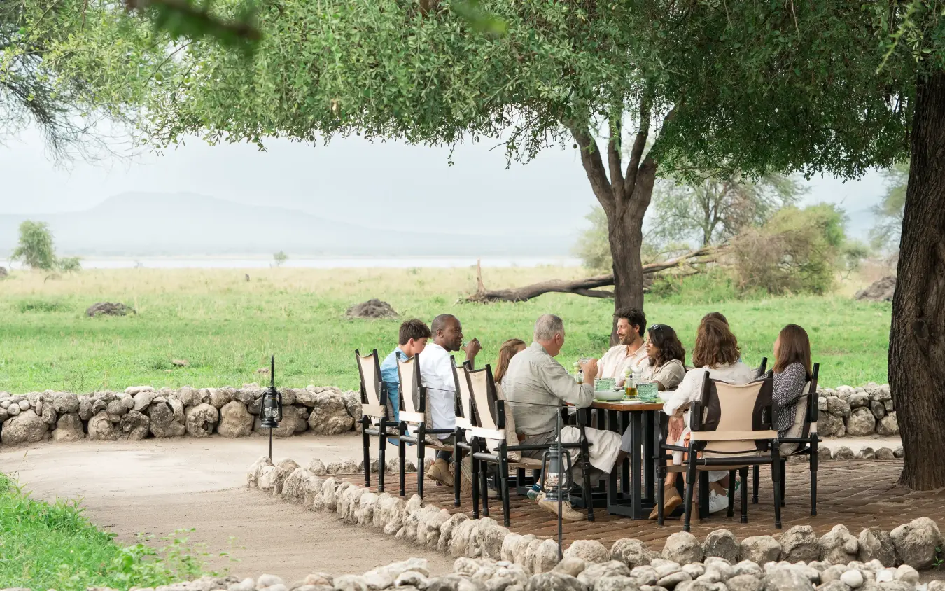 Guests dining outdoors under large tree with savanna views, Little Chem Chem, Lake Manyara, Tanzania