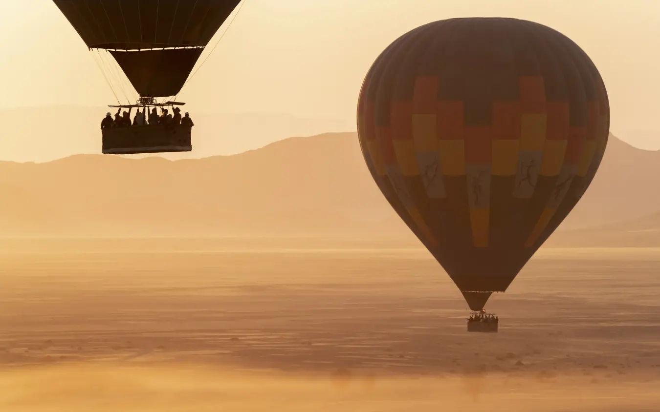 Two hot air balloons drifting over desert landscape at dawn, Little Kulala, Sossusvlei, Namibia