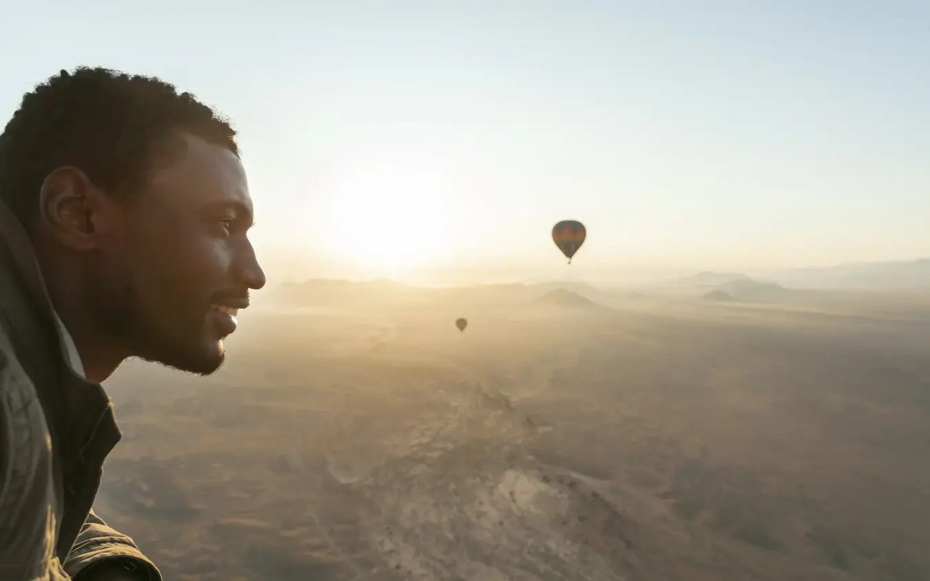 Man watching hot air balloons drift across desert landscape at dawn, Little Kulala, Sossusvlei, Namibia