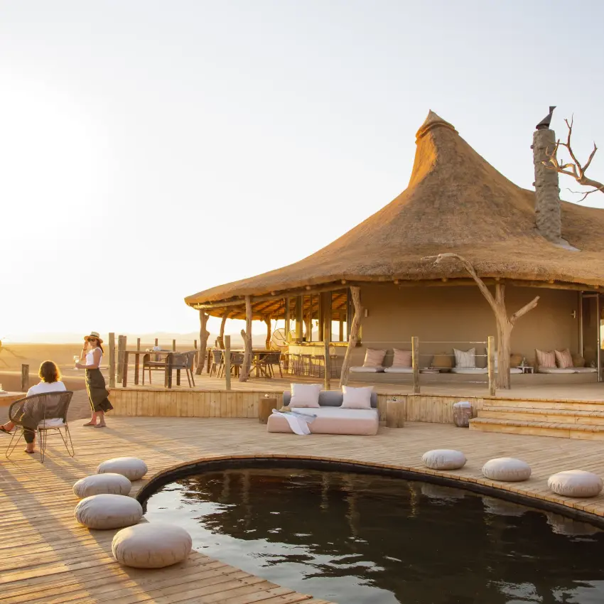Thatched pavilion with infinity pool at sunset overlooking plains, Little Kulala, Sossusvlei, Namibia