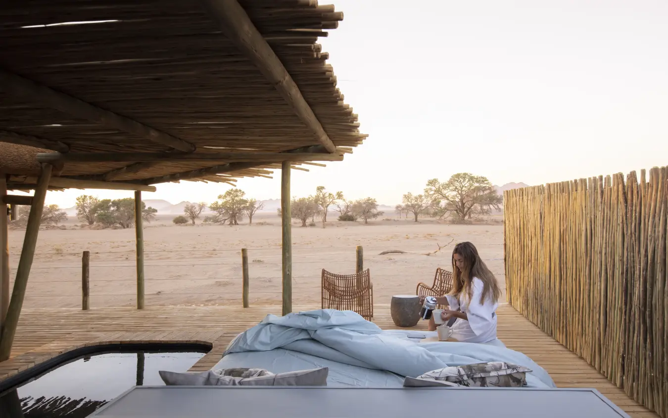 Woman relaxing on deck bed with savanna views at sunset, Little Kulala, Sossusvlei, Namibia