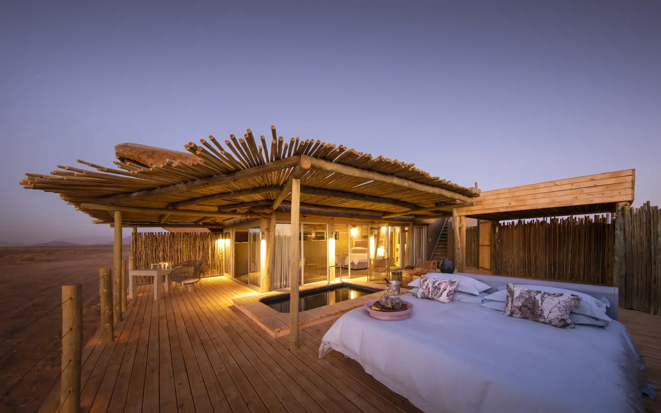 Luxury bedroom pavilion with outdoor bed on wooden deck at dusk, Little Kulala, Sossusvlei, Namibia