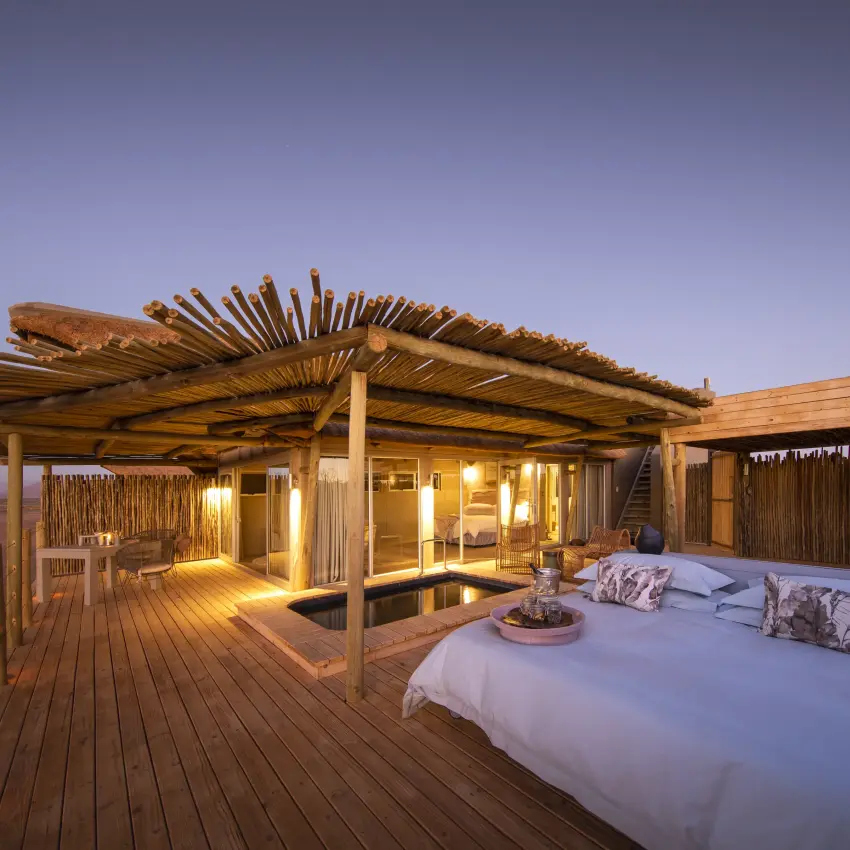 Luxury bedroom pavilion with outdoor bed on wooden deck at dusk, Little Kulala, Sossusvlei, Namibia