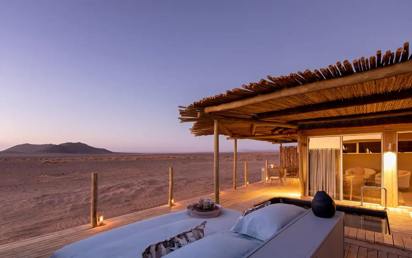 Luxury bedroom deck with bed overlooking desert landscape at dusk, Little Kulala, Sossusvlei, Namibia