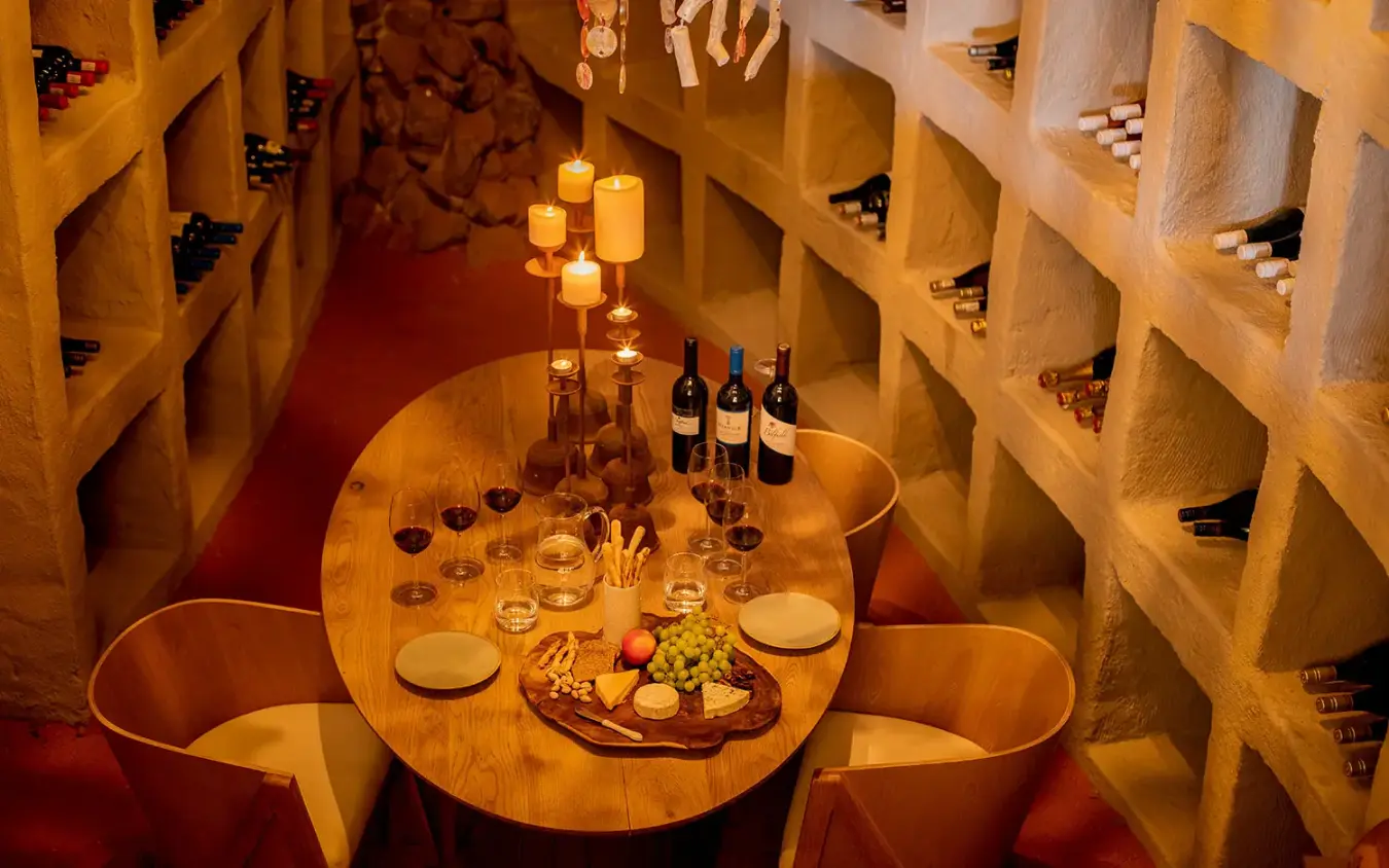 Wine cellar dining room with candlelit table and wine bottles displayed on shelves, Little Kulala, Sossusvlei, Namibia