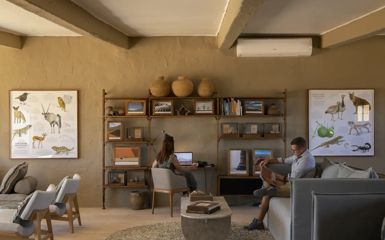 Modern lodge interior with wildlife artwork and guests working at desk, Little Kulala, Sossusvlei, Namibia
