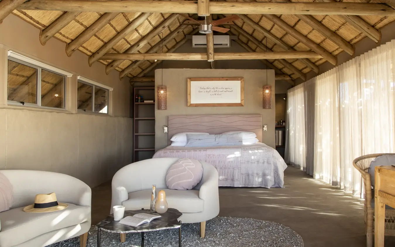 Luxury safari lodge bedroom with exposed timber beams and sitting area, Little Kulala, Sossusvlei, Namibia