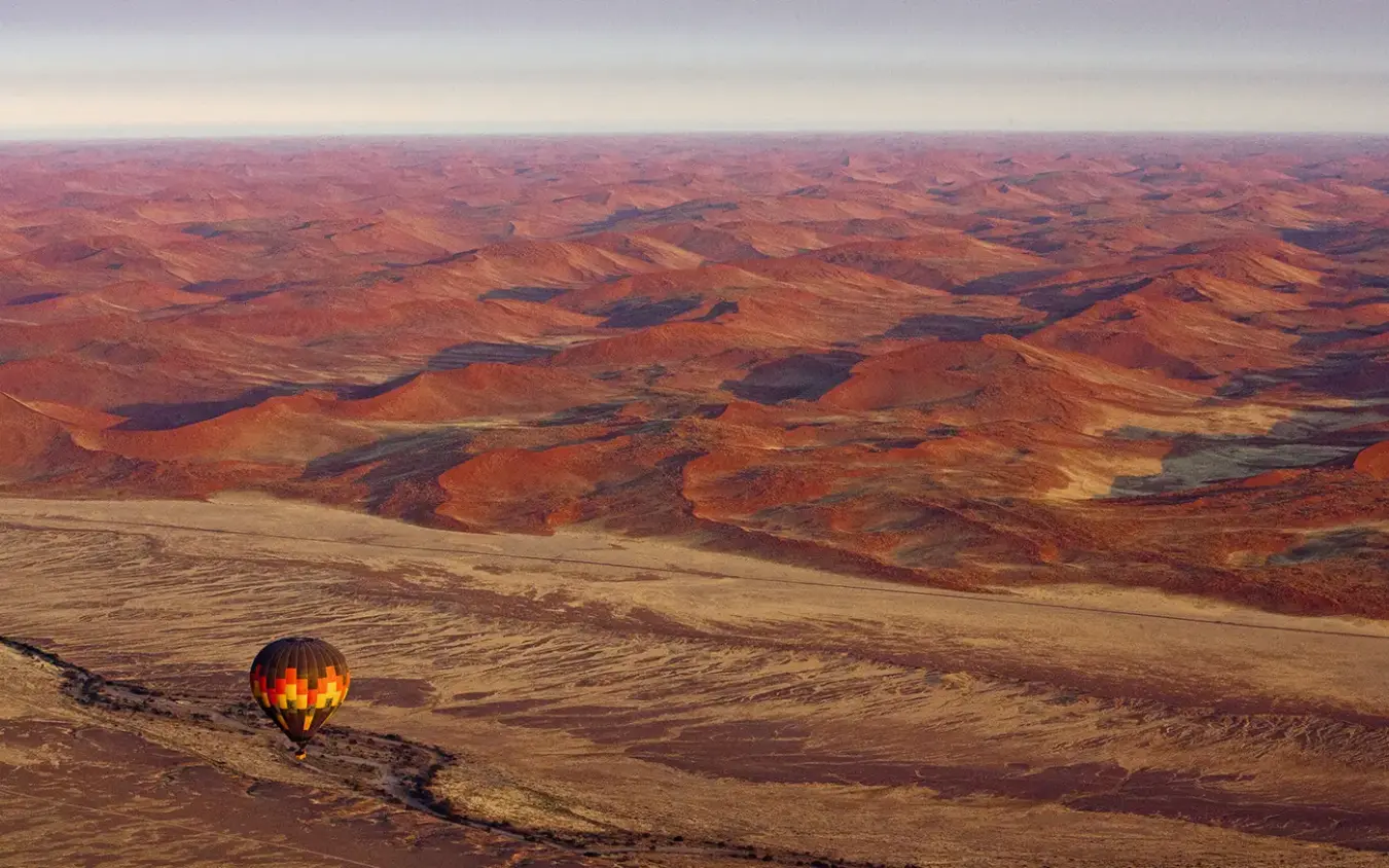 Hot air balloon drifting above arid desert landscape at dawn, Little Kulala, Sossusvlei, Namibia