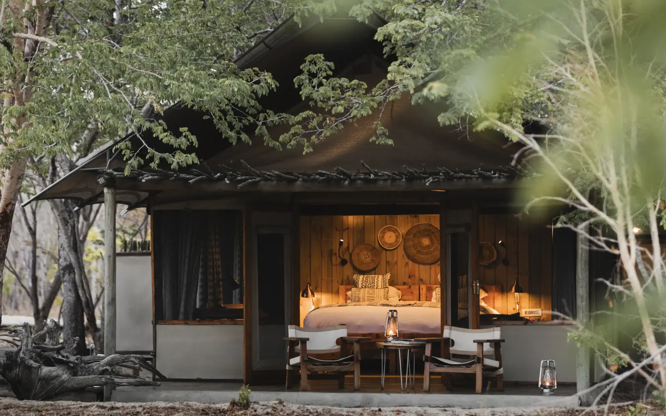 Luxury safari lodge bedroom with wooden finishes surrounded by trees at dusk, Little Makalolo, Hwange National Park, Zimbabwe