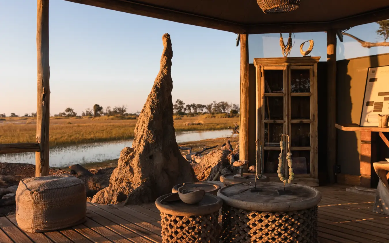 Safari lodge deck with termite mound and waterhole at golden hour, Little Vumbura, The Okavango Delta, Botswana