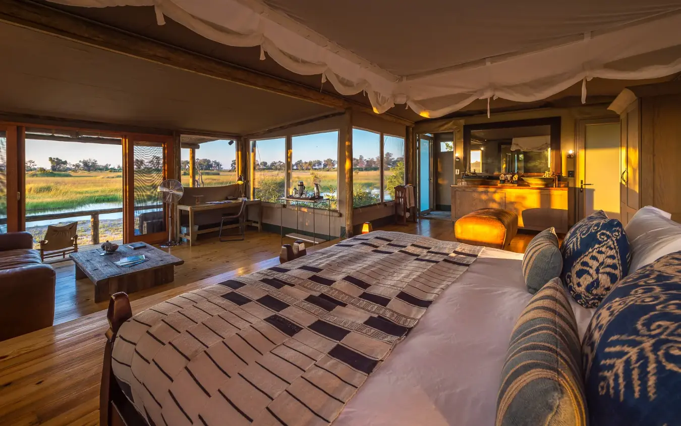 Luxury safari lodge bedroom with expansive windows overlooking wetland landscape at sunset, Little Vumbura, The Okavango Delta, Botswana