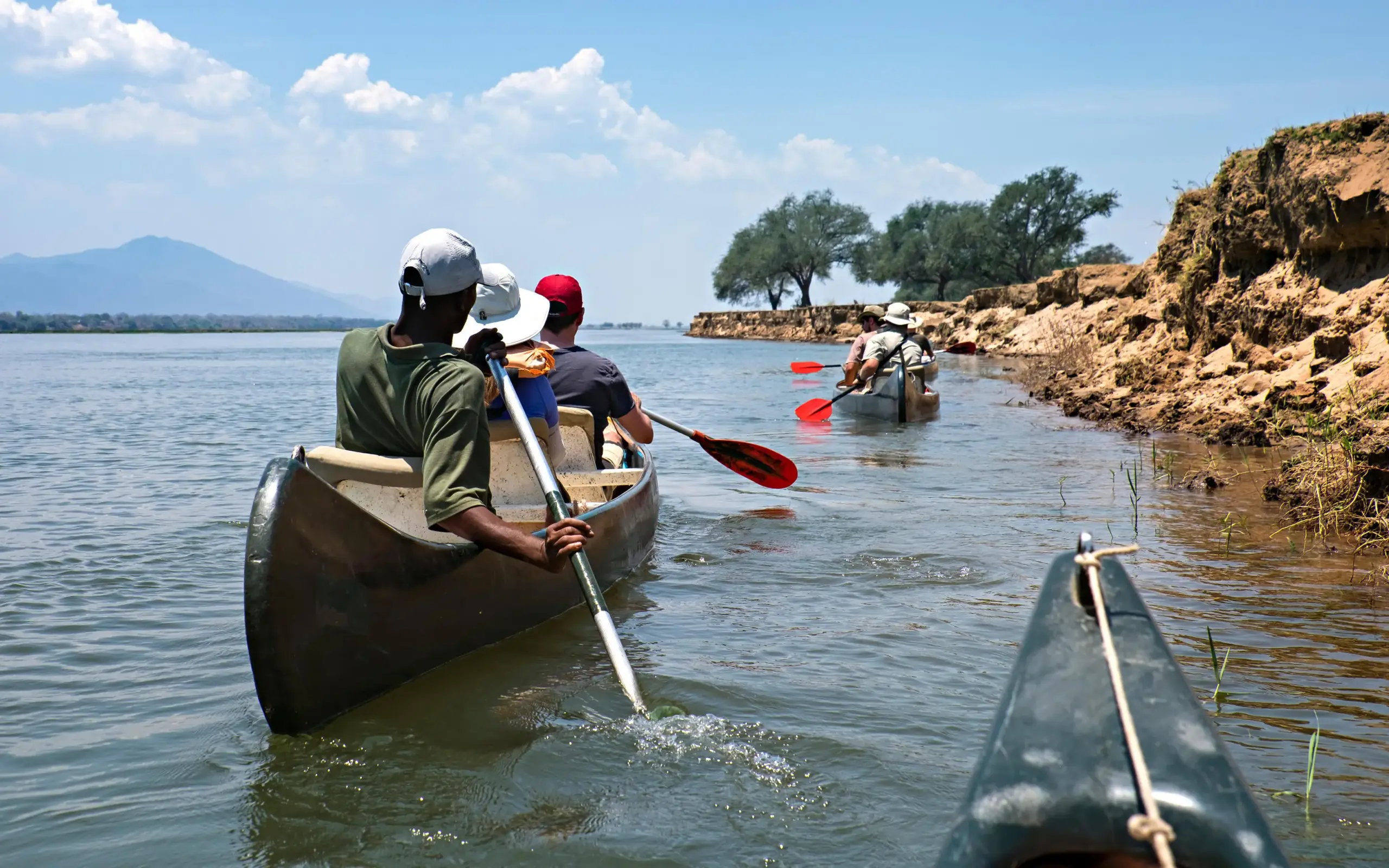 Guests paddling traditional canoes on calm water near shore, Zimbabwe