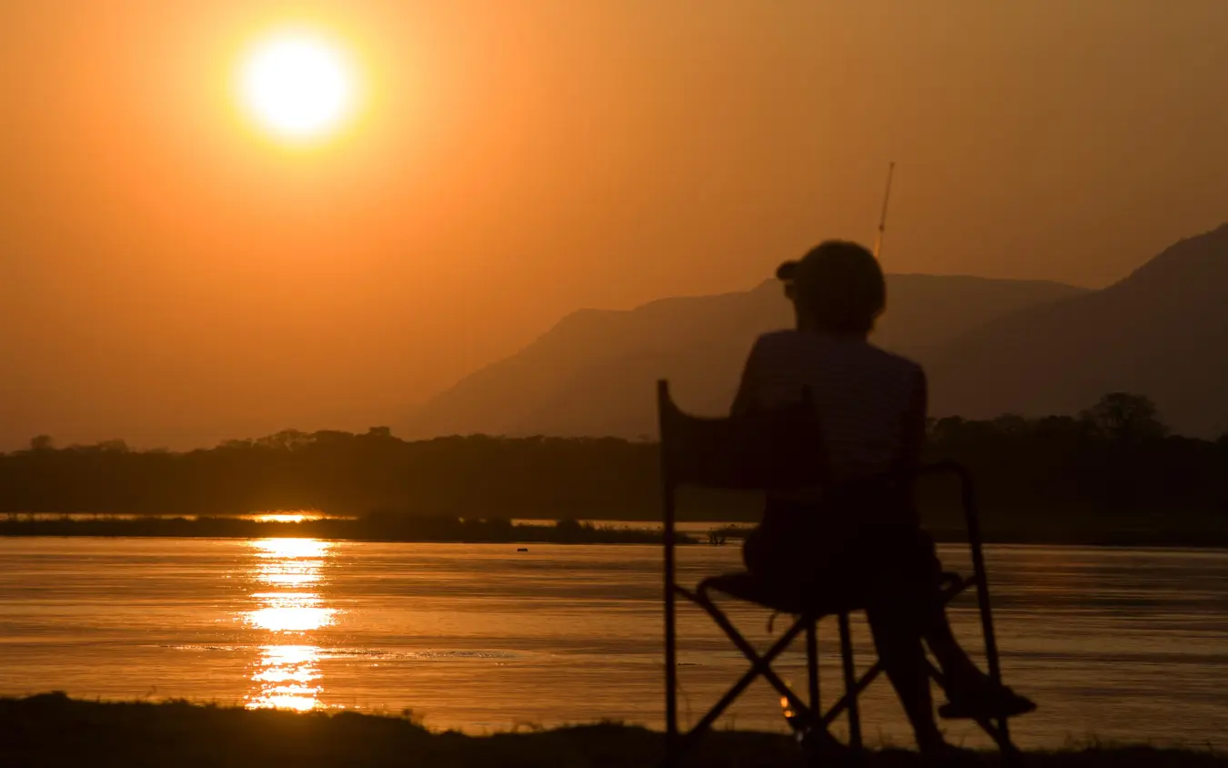 Person sitting by river at sunset watching wildlife, Little Vundu, Mana Pools, Zimbabwe