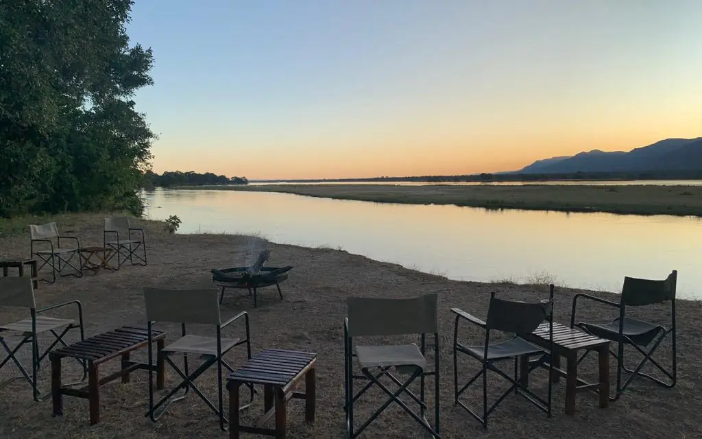 Riverside camp chairs and fire pit at sunset overlooking water, Little Vundu, Mana Pools, Zimbabwe