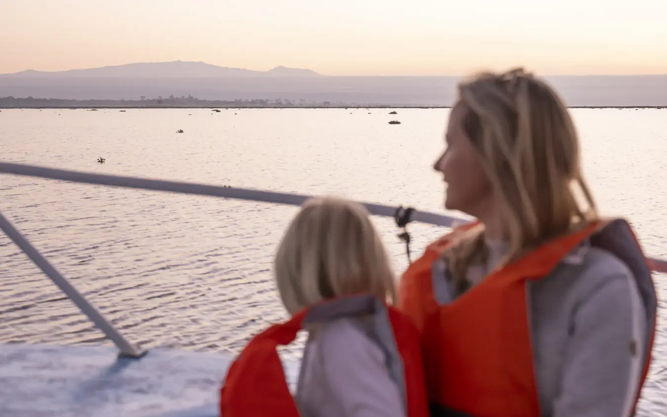 Woman and child in life jackets on boat viewing coastal landscape at dusk, Loldia House, Rift Valley Lakes, Kenya