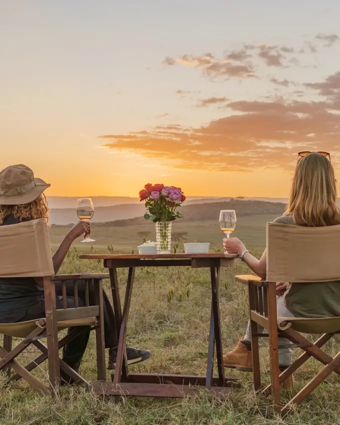 Two guests enjoying sunset wine service in savanna chairs overlooking grassland, Rift Valley Lakes, Kenya