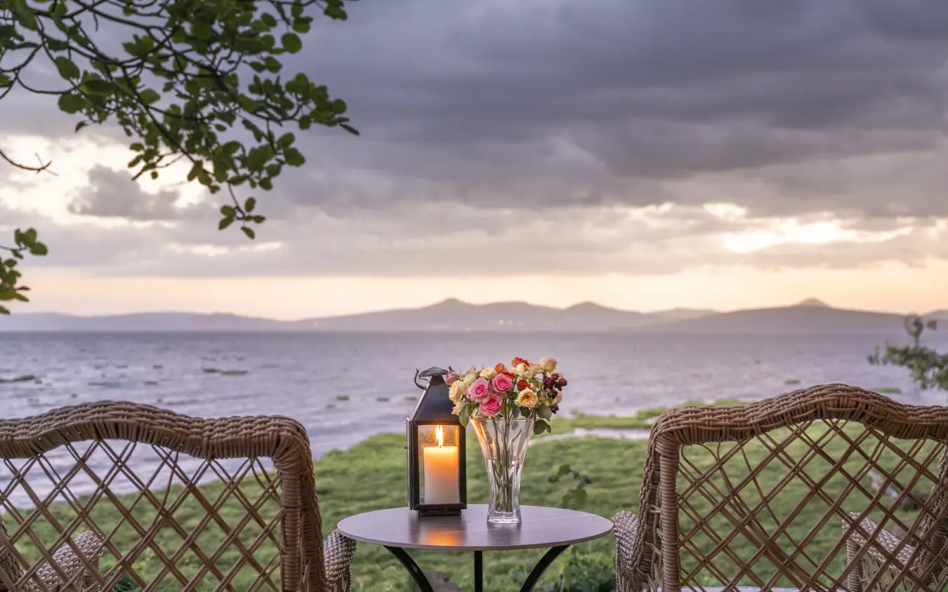 Wicker chairs with flowers and lantern overlooking coastal water at dusk, Loldia House, Rift Valley Lakes, Kenya