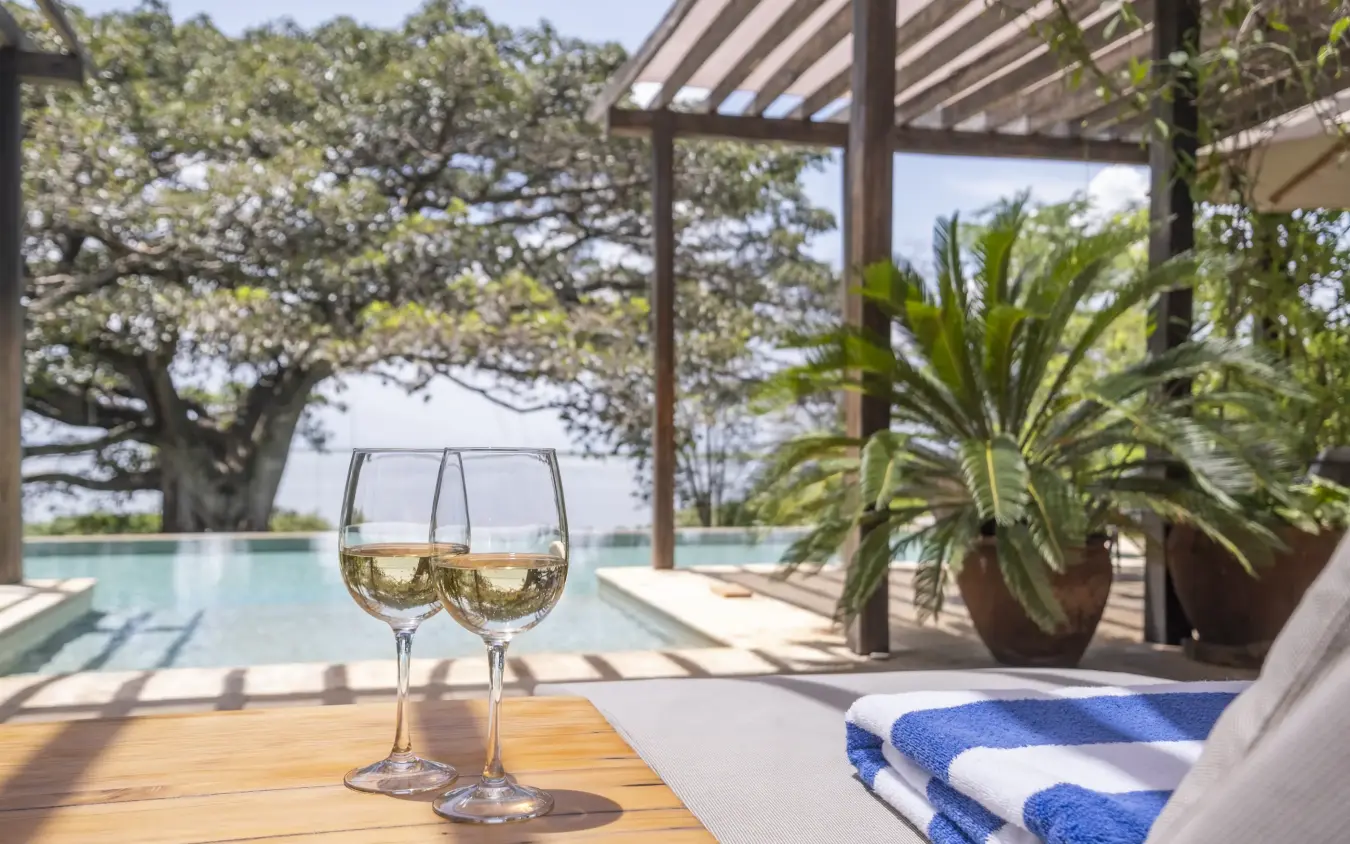 Two wine glasses on wooden deck overlooking infinity pool and trees, Loldia House, Rift Valley Lakes, Kenya
