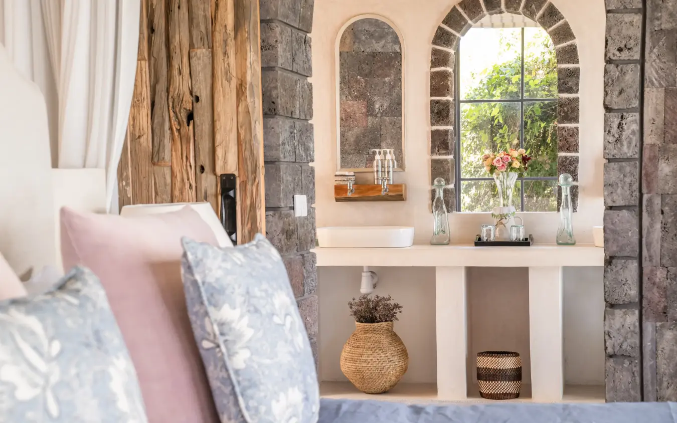 Bedroom interior with stone walls and arched window overlooking garden, Loldia House, Rift Valley Lakes, Kenya
