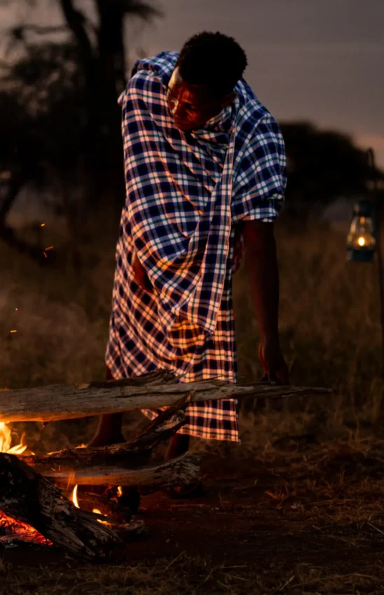 Person warming by campfire at dusk in savanna landscape, Lolkisale Camp, Tarangire National Park, Tanzania