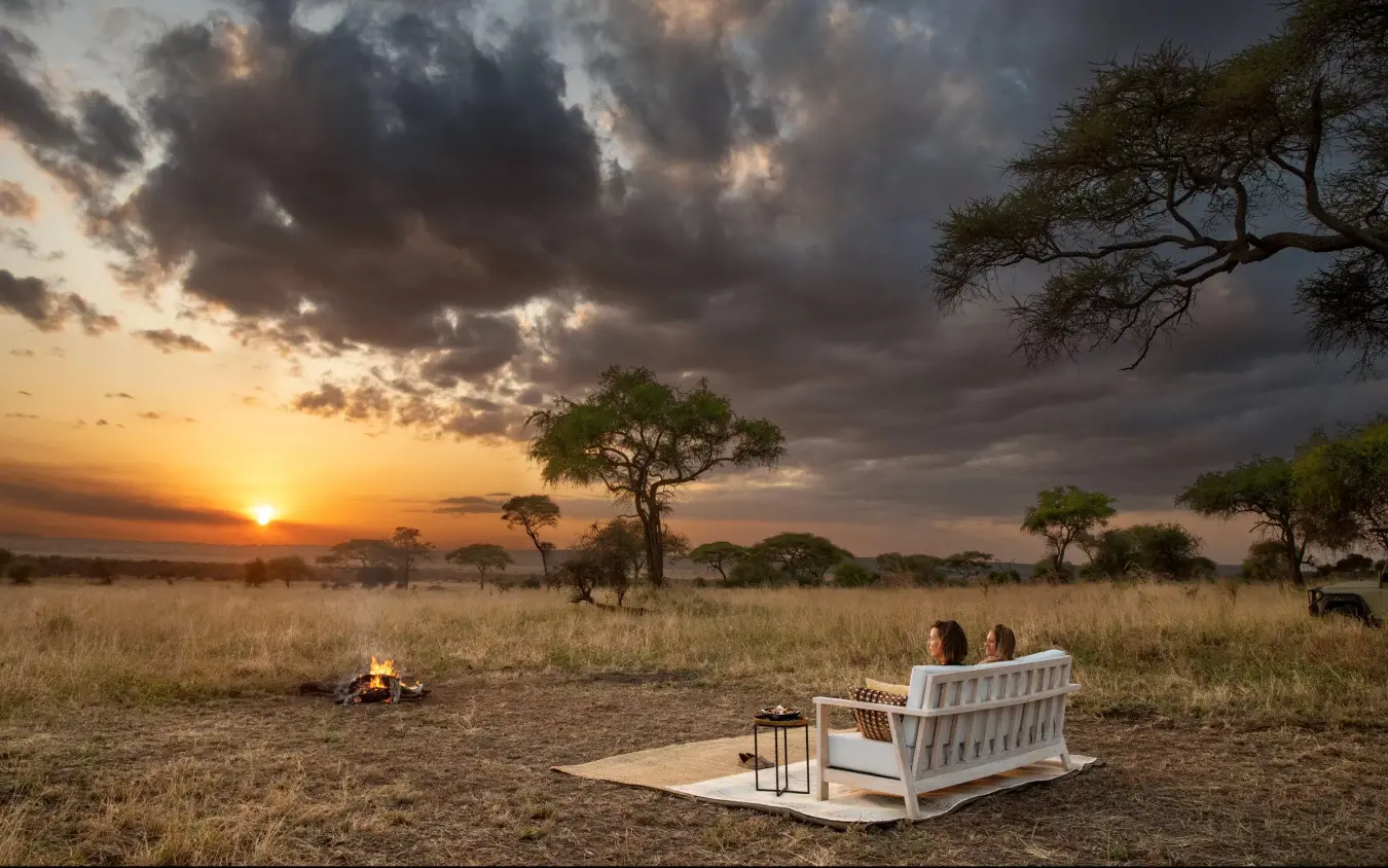 Guests relax on outdoor furniture at sunset with campfire, Lolkisale Camp, Tarangire National Park, Tanzania