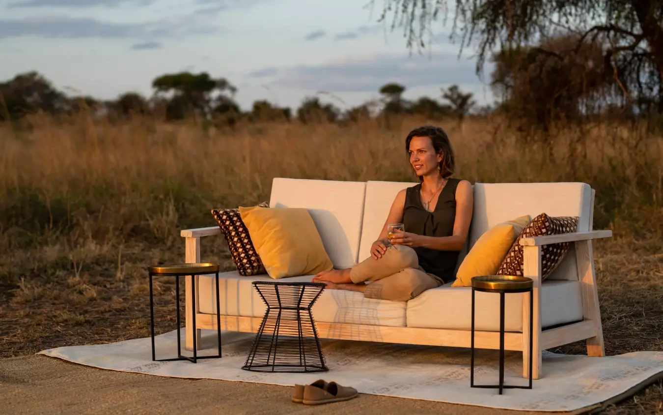 Woman relaxing on outdoor lounge furniture in savanna landscape, Lolkisale Camp, Tarangire National Park, Tanzania