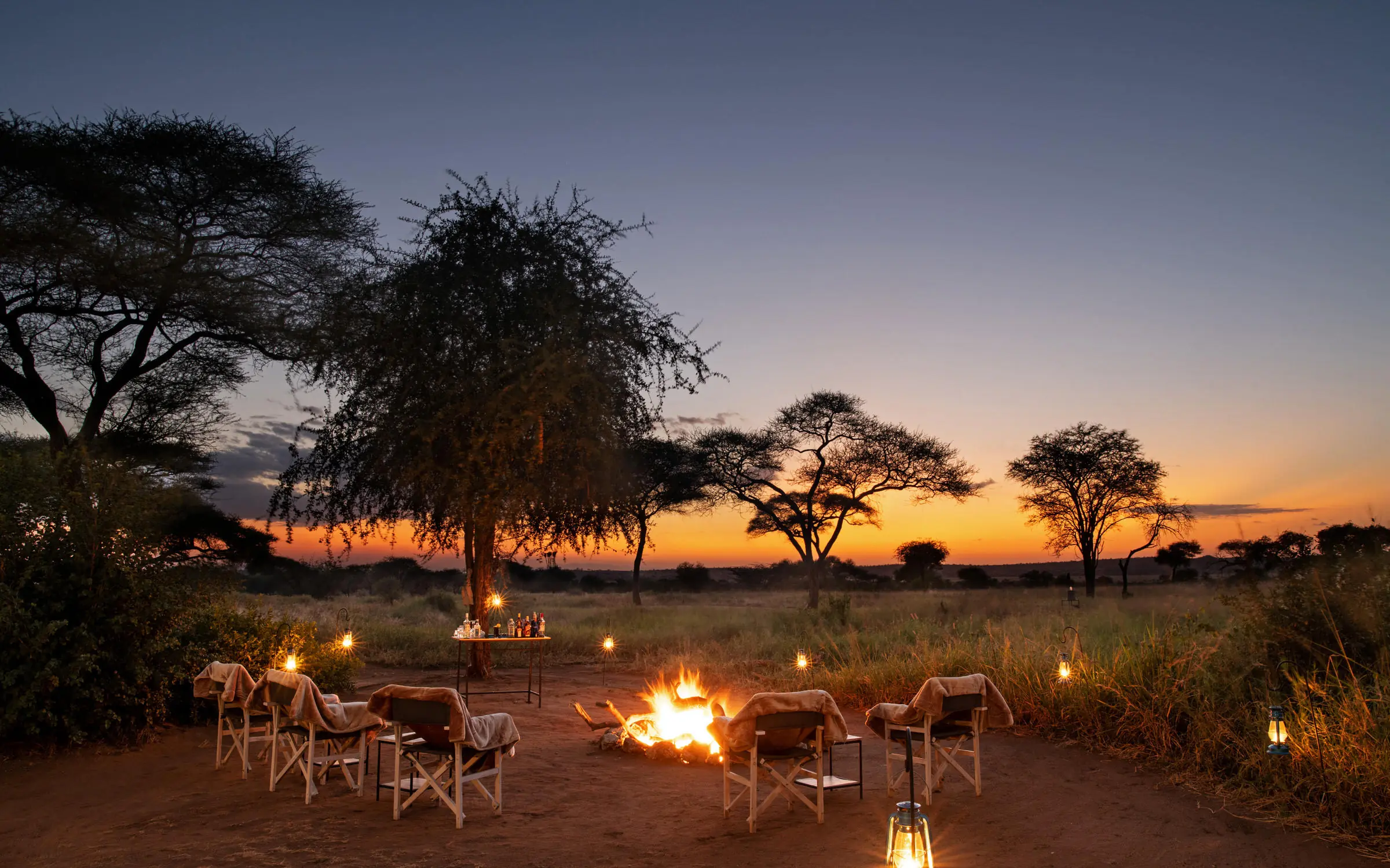 Evening campfire setup with chairs under acacia trees at sunset, Tanzania
