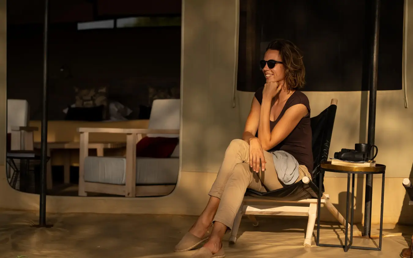 Woman in sunglasses relaxing on modern chair in lodge, Lolkisale Camp, Tarangire National Park, Tanzania