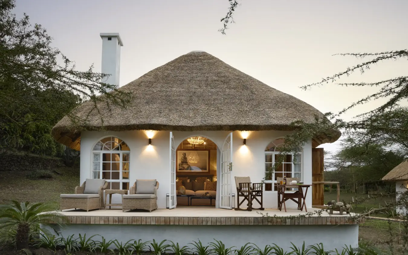 Thatched-roof lodge with white walls and lit interior at dusk, Mama Simba, Arusha, Tanzania