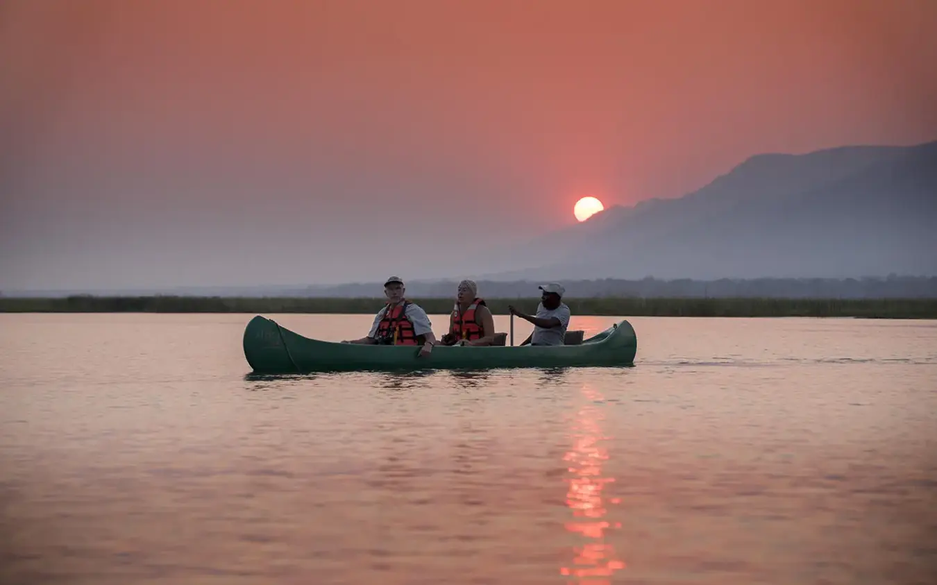 Guests paddling canoe on river at sunset with mountains, Zambezi Expeditions, Mana Pools, Zimbabwe